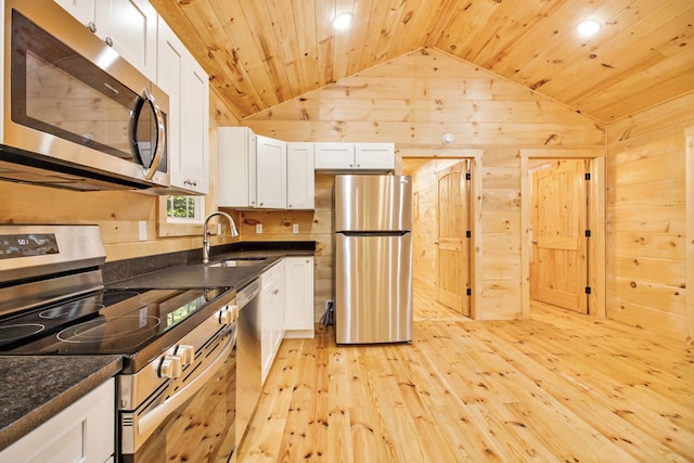 kitchen featuring wood walls, stainless steel appliances, sink, white cabinetry, and light wood-type flooring