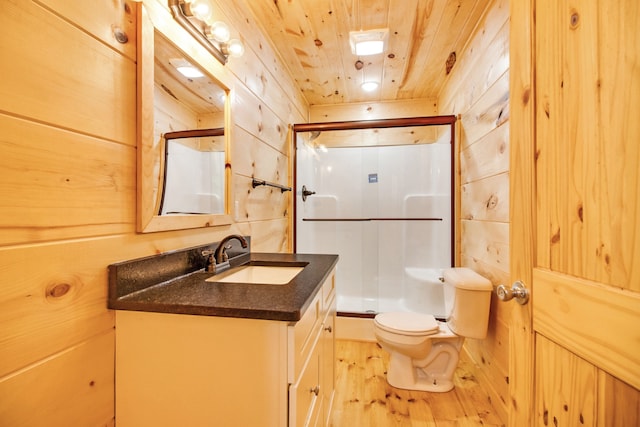 bathroom with a shower with shower door, toilet, wooden walls, and vanity