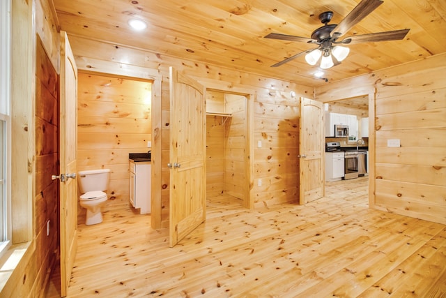 interior space with toilet, wood-type flooring, ceiling fan, and wooden walls