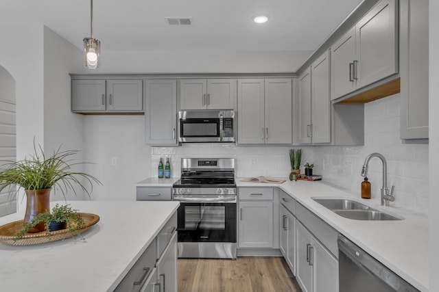 kitchen featuring pendant lighting, sink, backsplash, stainless steel appliances, and light wood-type flooring