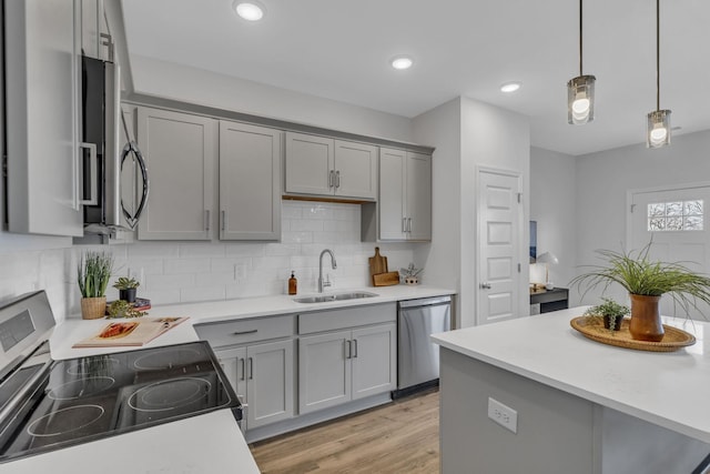 kitchen with sink, light wood-type flooring, appliances with stainless steel finishes, gray cabinets, and pendant lighting