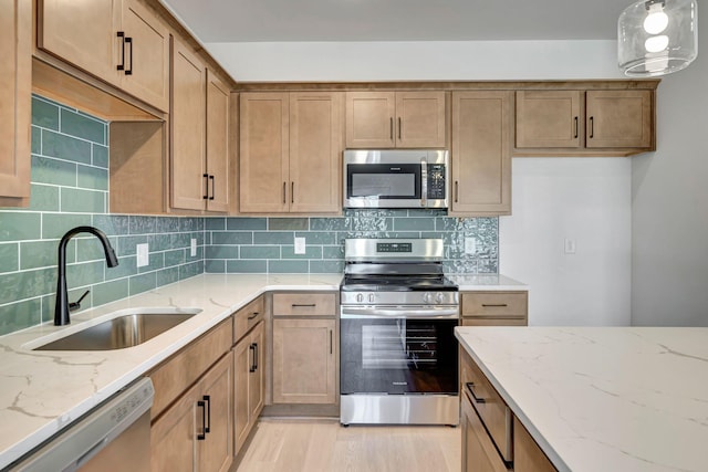 kitchen with sink, light stone counters, light wood-type flooring, stainless steel appliances, and decorative backsplash