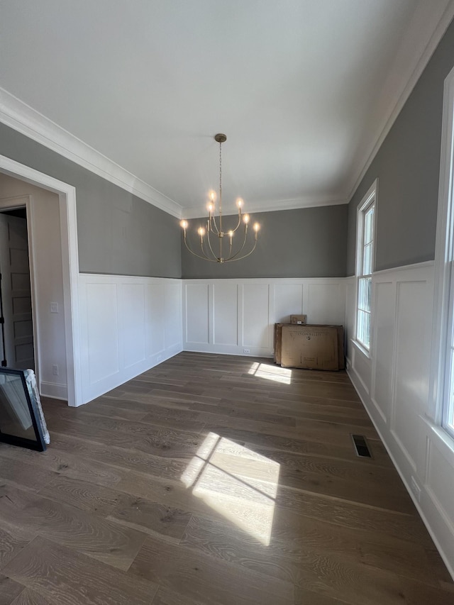 unfurnished dining area featuring ornamental molding, dark wood-type flooring, and a notable chandelier