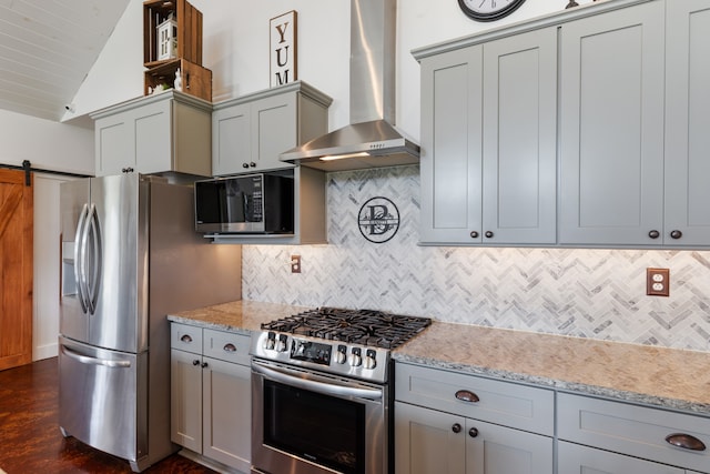 kitchen featuring appliances with stainless steel finishes, a barn door, wall chimney exhaust hood, vaulted ceiling, and tasteful backsplash