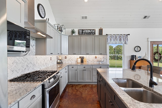 kitchen with decorative backsplash, appliances with stainless steel finishes, light stone countertops, wall chimney exhaust hood, and sink