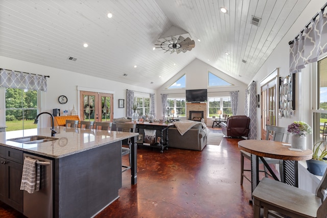 kitchen with a center island with sink, a fireplace, stainless steel dishwasher, light stone countertops, and sink