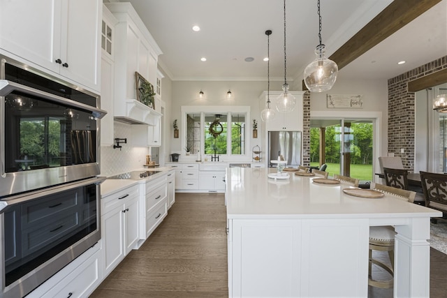 kitchen featuring appliances with stainless steel finishes, white cabinetry, a breakfast bar area, a large island with sink, and a healthy amount of sunlight