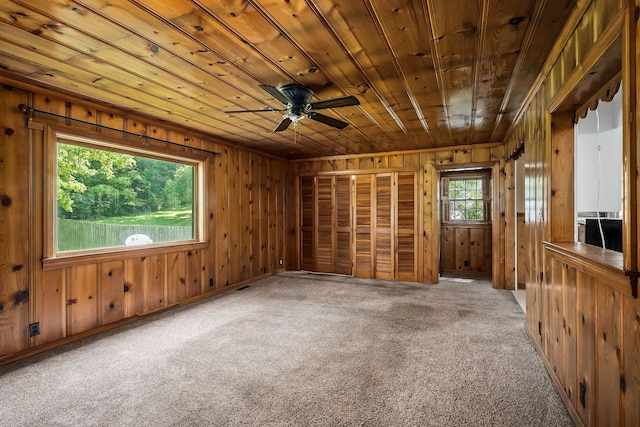 carpeted spare room featuring ceiling fan, wooden walls, and wood ceiling