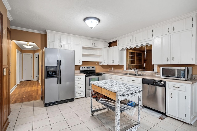 kitchen with sink, light tile patterned floors, ornamental molding, appliances with stainless steel finishes, and white cabinets