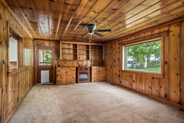 unfurnished living room with wooden walls, carpet flooring, ceiling fan, wood ceiling, and built in shelves