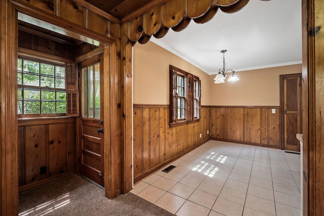 tiled empty room with crown molding, an inviting chandelier, and wood walls