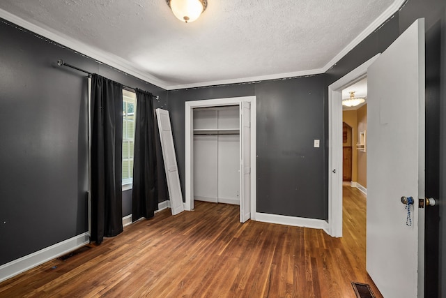 unfurnished bedroom featuring a textured ceiling, ornamental molding, hardwood / wood-style floors, and a closet