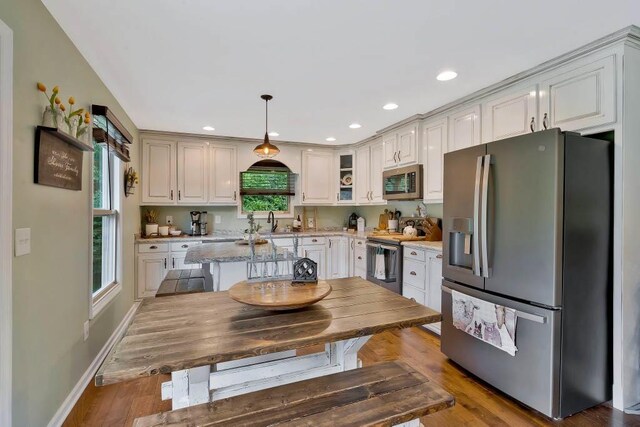 kitchen with sink, hanging light fixtures, stainless steel appliances, light stone countertops, and hardwood / wood-style floors