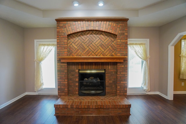 unfurnished living room featuring dark hardwood / wood-style flooring, a raised ceiling, and a brick fireplace