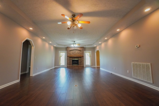 unfurnished living room with ceiling fan, dark hardwood / wood-style floors, a textured ceiling, and a brick fireplace