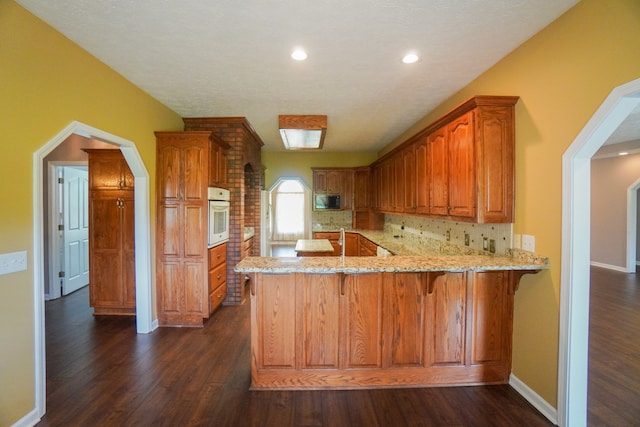 kitchen with decorative backsplash, dark wood-type flooring, oven, and kitchen peninsula