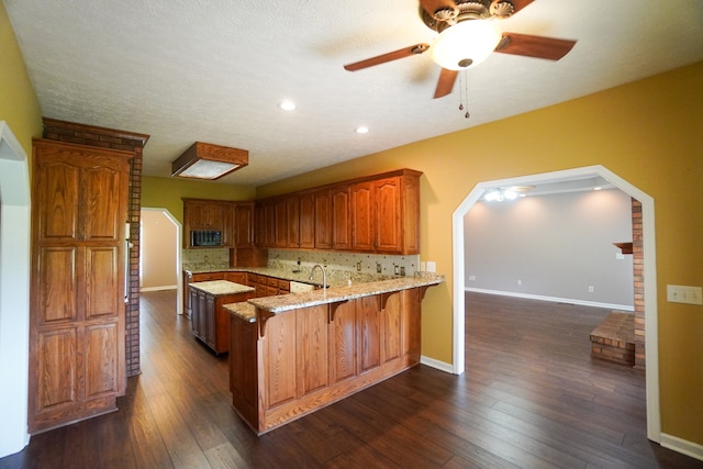 kitchen with a kitchen breakfast bar, dark hardwood / wood-style floors, kitchen peninsula, light stone countertops, and backsplash