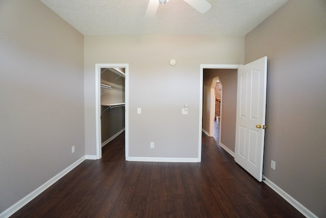 unfurnished bedroom featuring a walk in closet, ceiling fan, dark wood-type flooring, a textured ceiling, and a closet