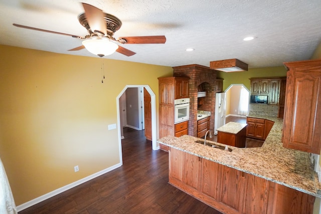 kitchen featuring sink, dark hardwood / wood-style flooring, light stone counters, kitchen peninsula, and white appliances