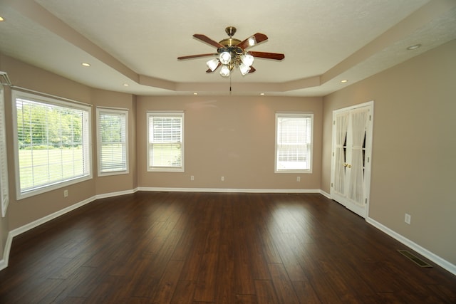 unfurnished room featuring a healthy amount of sunlight, dark hardwood / wood-style flooring, and a tray ceiling