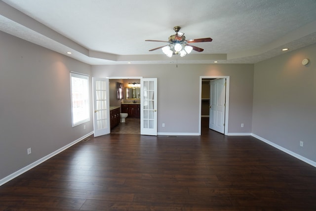 spare room featuring a textured ceiling, dark wood-type flooring, french doors, and a raised ceiling