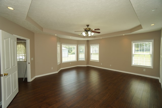 empty room with dark hardwood / wood-style floors, a tray ceiling, and a wealth of natural light