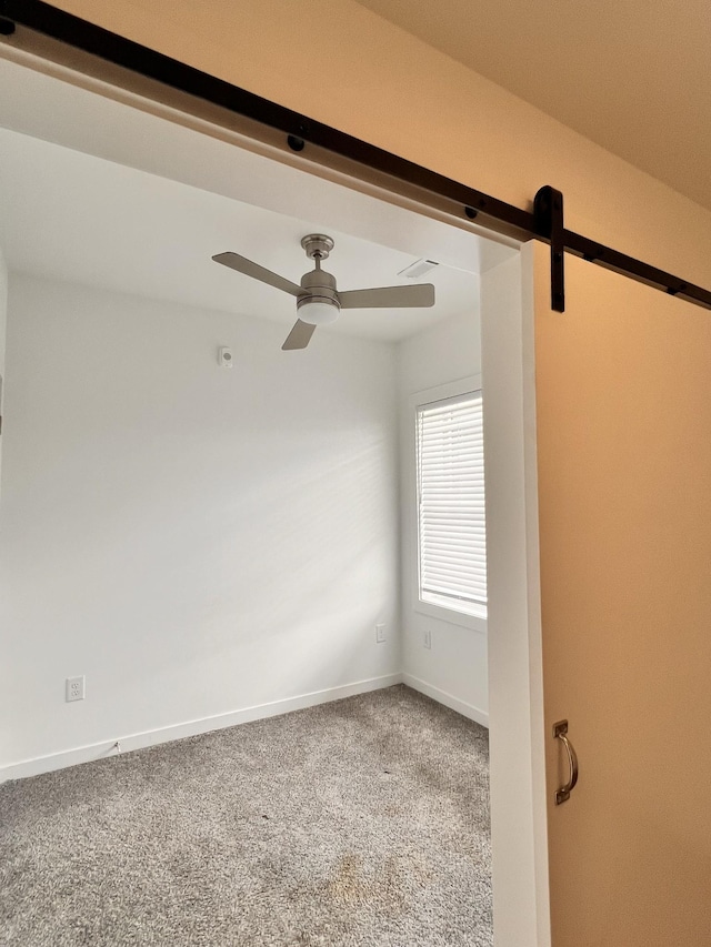 empty room featuring carpet floors, a ceiling fan, baseboards, and a barn door