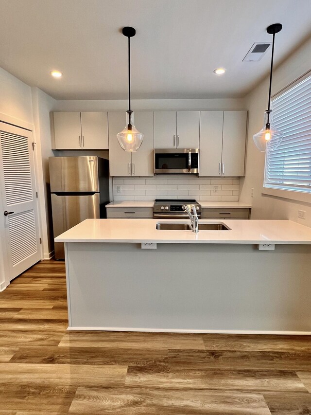 kitchen featuring backsplash, stainless steel appliances, pendant lighting, and light hardwood / wood-style floors