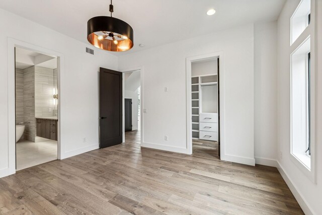 unfurnished bedroom featuring wood-type flooring, a walk in closet, ensuite bathroom, and a closet