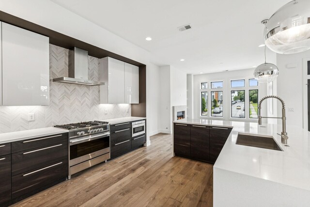 kitchen featuring tasteful backsplash, hardwood / wood-style floors, white cabinets, wall chimney exhaust hood, and stainless steel appliances