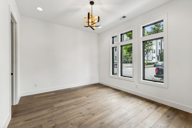 empty room with hardwood / wood-style floors and a chandelier