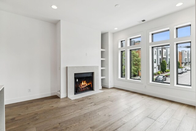 unfurnished living room with built in features and light hardwood / wood-style floors