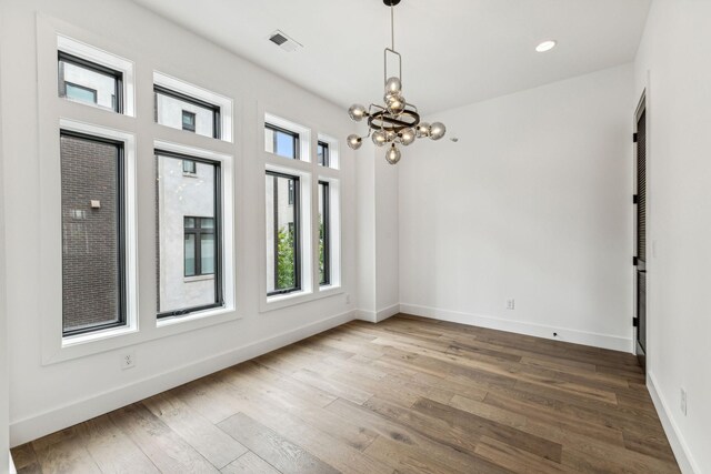 unfurnished room with an inviting chandelier and hardwood / wood-style flooring