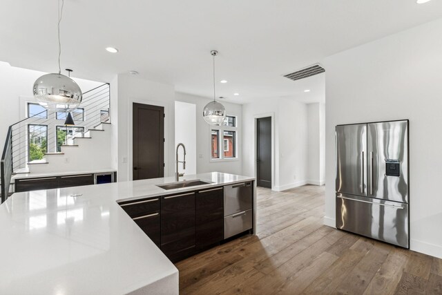 kitchen featuring dark hardwood / wood-style floors, decorative light fixtures, an island with sink, stainless steel appliances, and sink