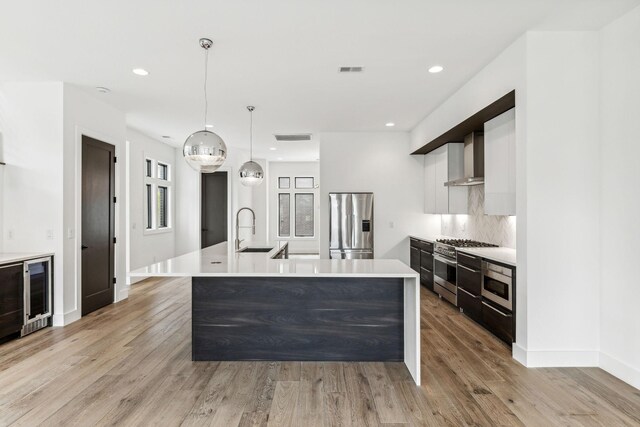 kitchen featuring light hardwood / wood-style flooring, white cabinetry, appliances with stainless steel finishes, wall chimney range hood, and pendant lighting