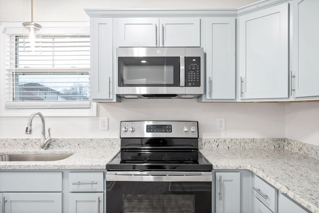 kitchen with appliances with stainless steel finishes, sink, hanging light fixtures, and light stone countertops