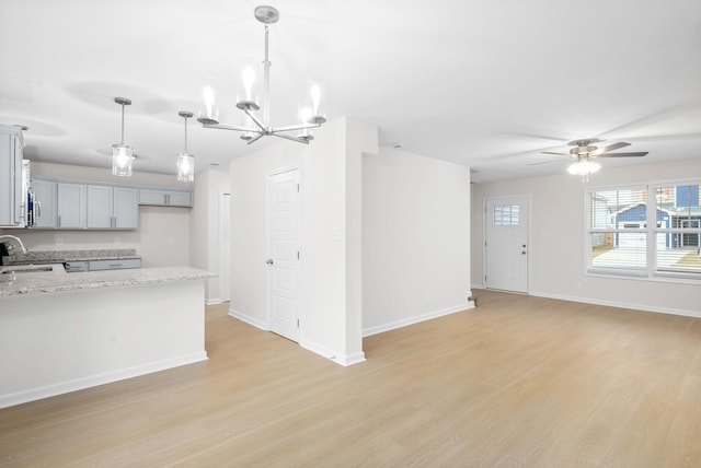 kitchen featuring sink, gray cabinets, light hardwood / wood-style floors, hanging light fixtures, and light stone countertops