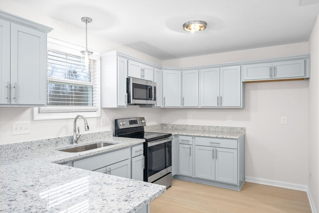 kitchen featuring appliances with stainless steel finishes, sink, light stone counters, light wood-type flooring, and decorative light fixtures