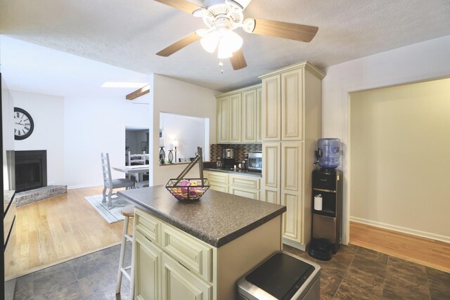 kitchen with dark hardwood / wood-style floors, ceiling fan, cream cabinetry, a brick fireplace, and tasteful backsplash