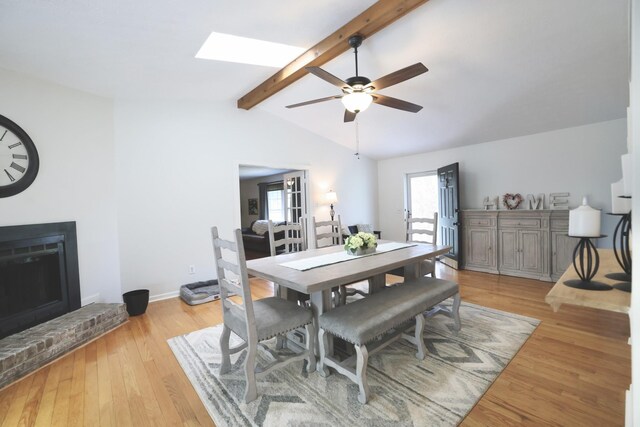 dining room featuring ceiling fan, vaulted ceiling with skylight, a fireplace, and light hardwood / wood-style floors