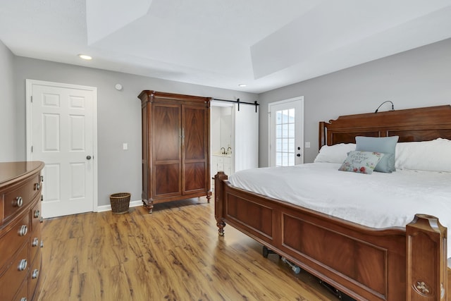 bedroom featuring light wood-type flooring, a raised ceiling, and a barn door