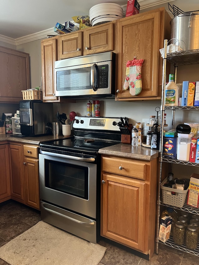 kitchen with dark tile patterned flooring, appliances with stainless steel finishes, and ornamental molding