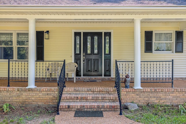 entrance to property featuring covered porch and roof with shingles