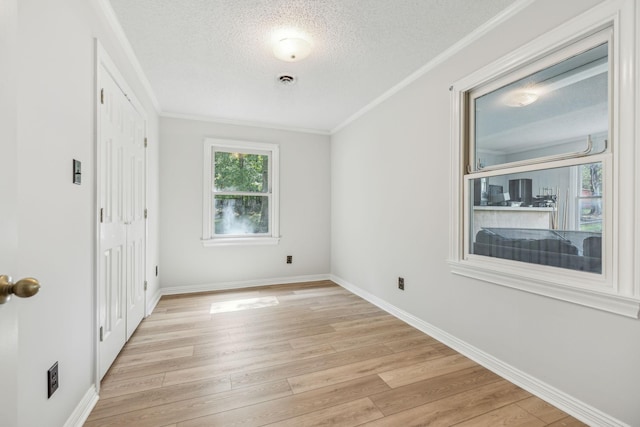 unfurnished room with crown molding, baseboards, light wood-type flooring, and a textured ceiling