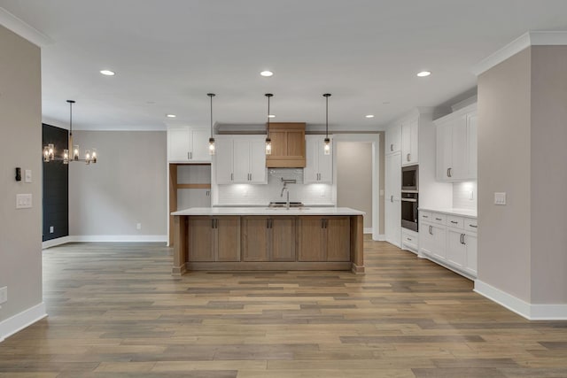 kitchen with wood finished floors, a sink, decorative backsplash, light countertops, and ornamental molding