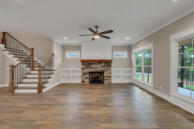 unfurnished living room featuring a stone fireplace, hardwood / wood-style floors, ceiling fan, and crown molding