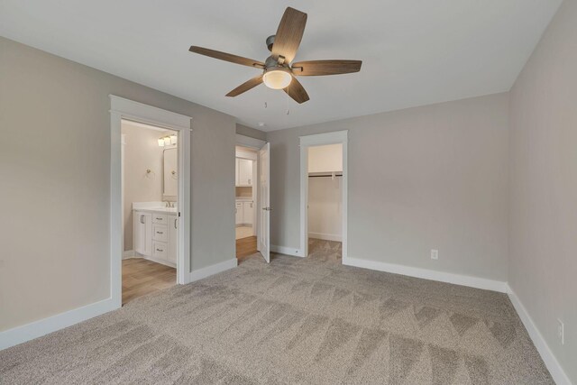 unfurnished bedroom with a spacious closet, ceiling fan, connected bathroom, and light carpet