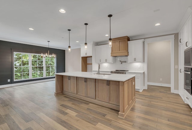 kitchen featuring tasteful backsplash, premium range hood, light wood-style floors, and a sink