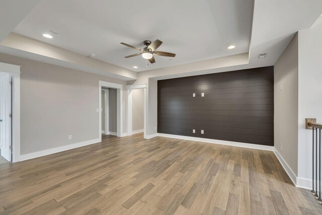 spare room with light hardwood / wood-style flooring, ceiling fan, and a raised ceiling