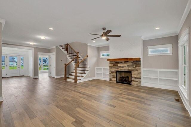 unfurnished living room with hardwood / wood-style flooring, a stone fireplace, ornamental molding, and ceiling fan